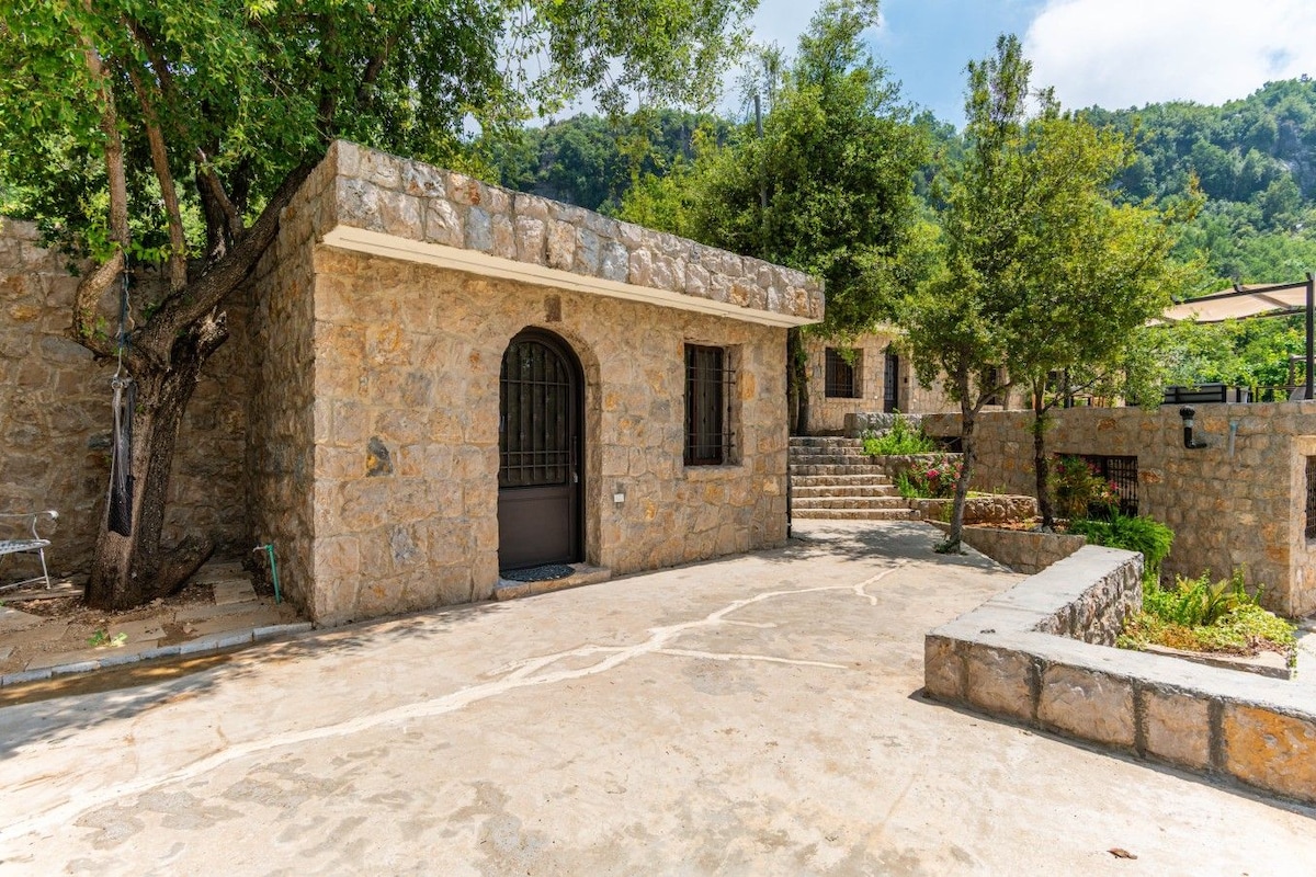 Edifício de pedra com uma porta central arqueada, uma pequena escadaria que leva a um andar superior e um pátio pavimentado.