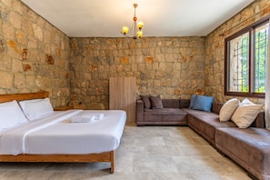 Quarto com parede de pedra, cama, sofá e janela.