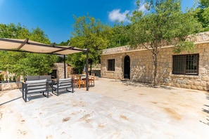 Um pátio externo com piso de pedra, pérgola e um edifício de pedra com porta em arco.