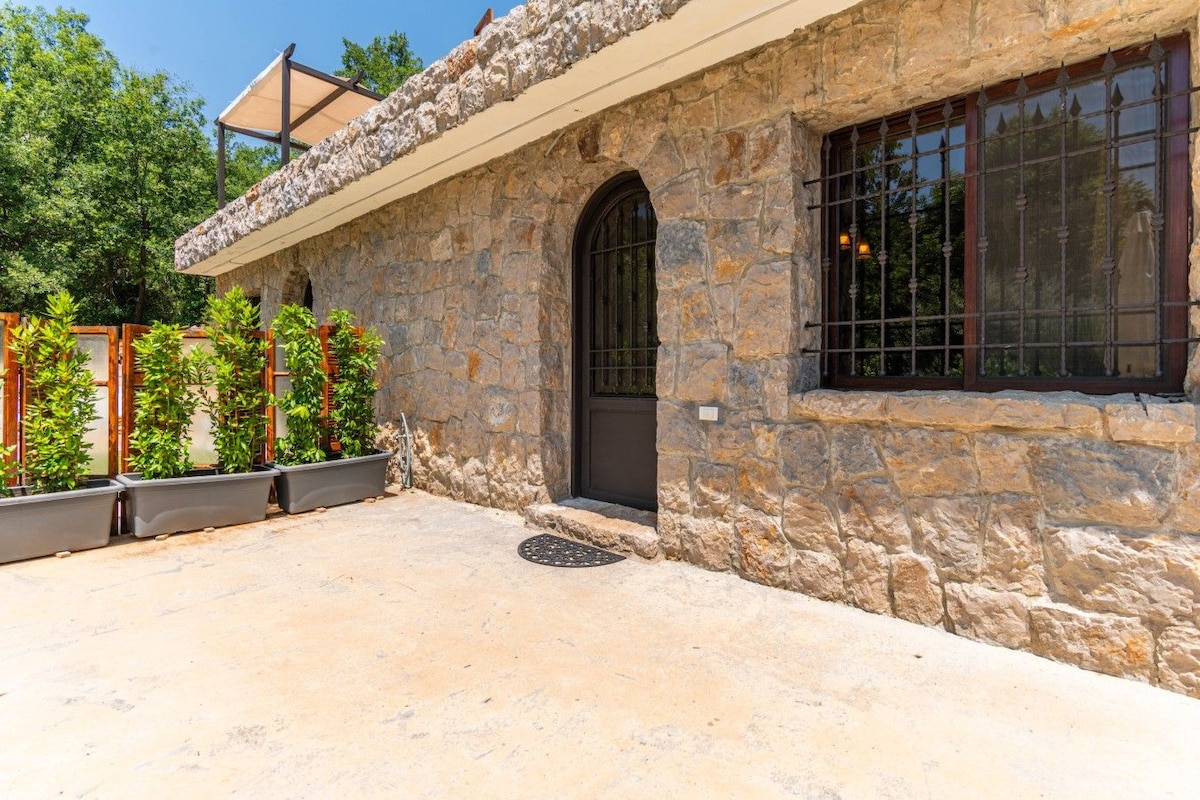 Um edifício de pedra com entrada em arco escura, uma janela com grades de metal e uma área de pátio coberta com vasos de plantas.