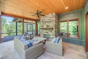 A covered outdoor seating area with wicker furniture and a stone fireplace. - Welcome to Kingfisher- Your Lake James Escape! (Nebo)