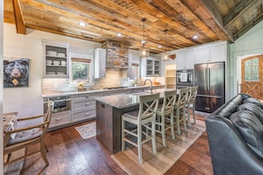 A kitchen with a central island, bar stools, a refrigerator, and a stone accent wall. - Welcome to Kingfisher- Your Lake James Escape! (Nebo)
