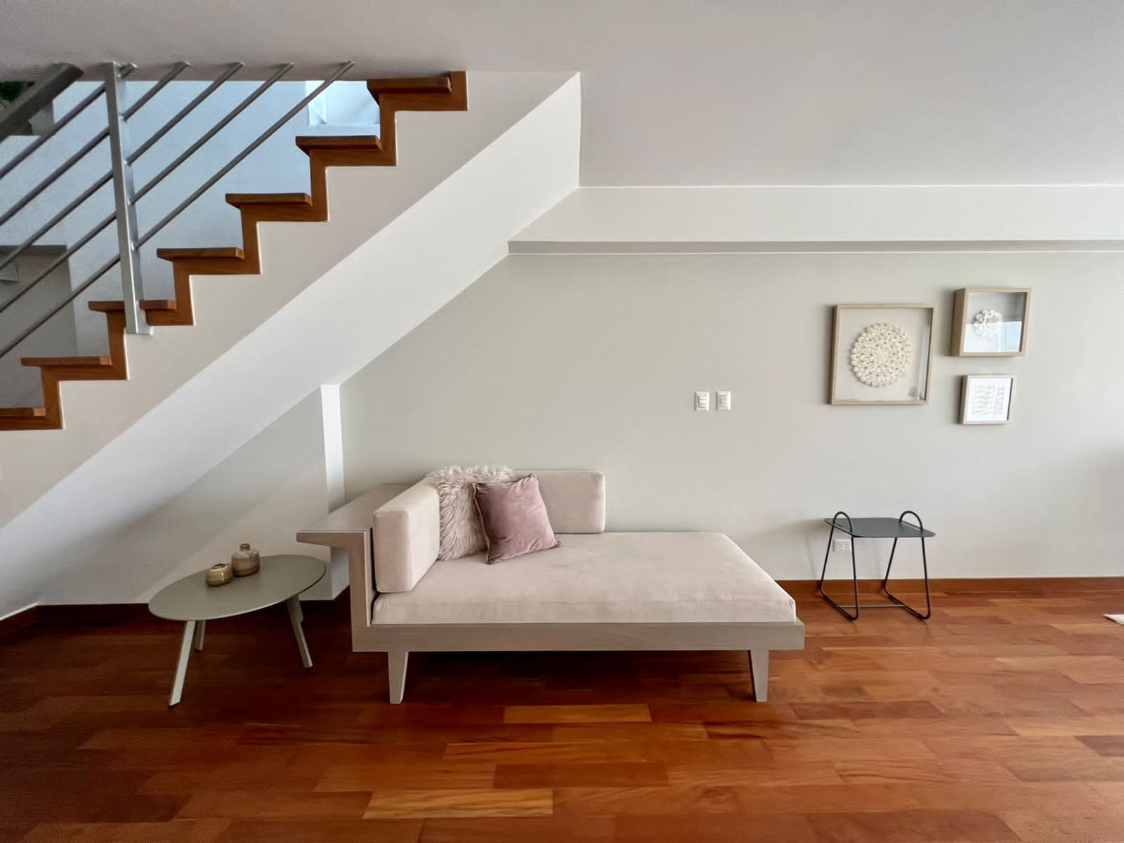 A modern living room with a sofa, a small table, a staircase, and a wall with framed artwork.