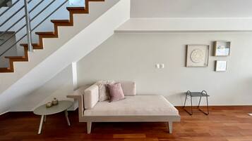 Una sala de estar moderna con un sofá, una mesita, una escalera y una pared decorada con cuadros.