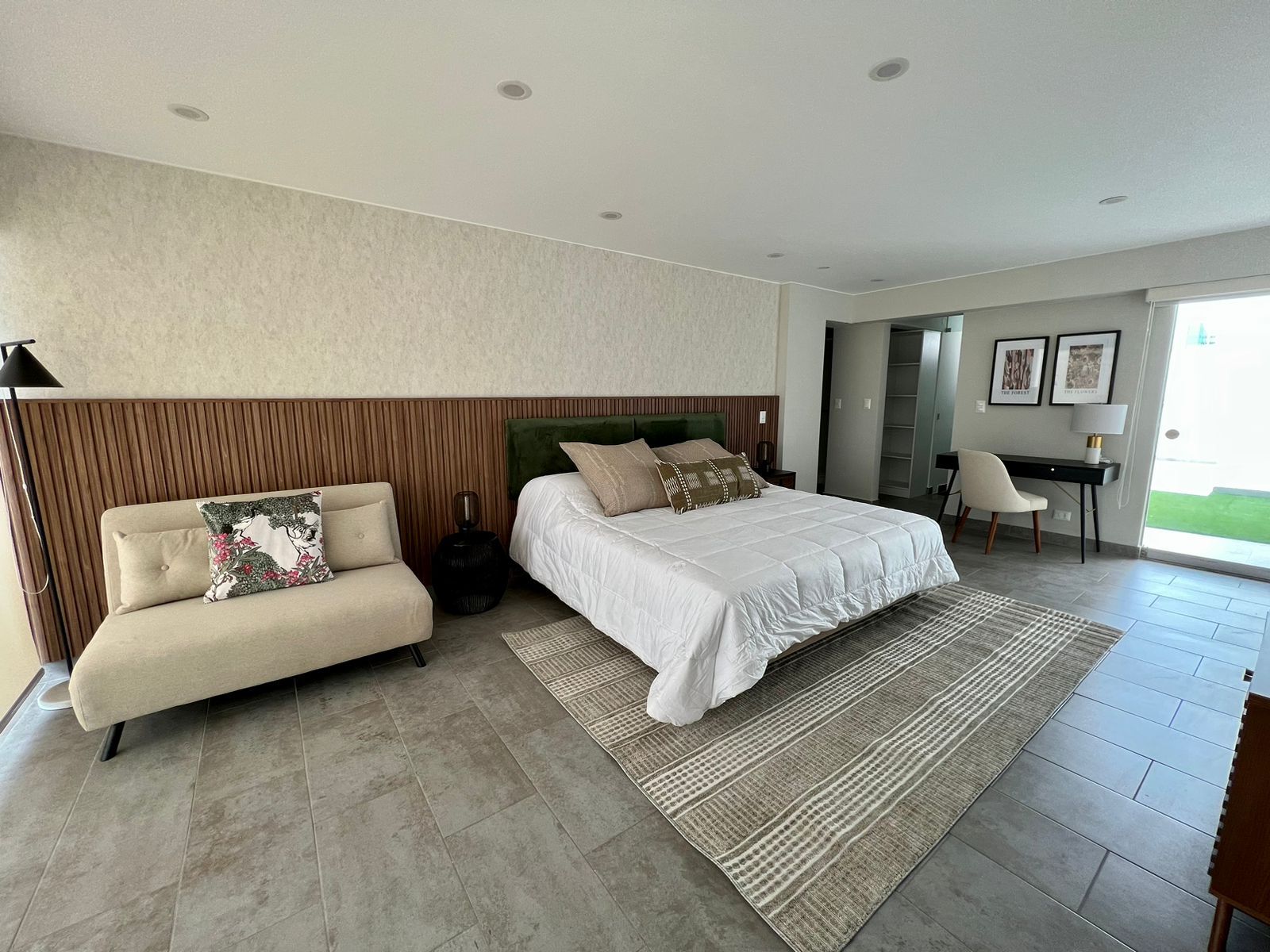 A modern bedroom with a bed, a sofa, a desk, and a view of the outdoors.