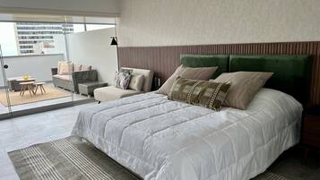 A modern bedroom with a large bed, a sofa, and a dining area with a table and chairs.
