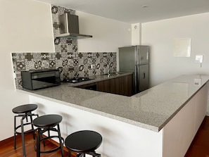 Una cocina moderna con microondas integrado, estufa a gas, refrigerador de acero inoxidable y un salpicadero con diseño. Hay dos taburetes de bar en la isla.