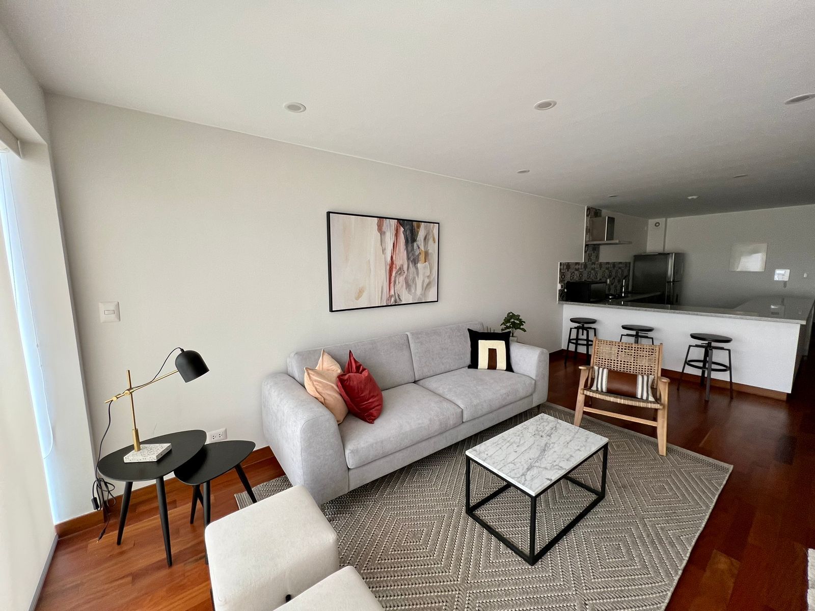A modern living room with a grey sofa, a coffee table, and a dining area with bar stools.