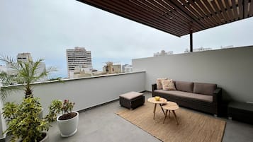 Una terraza en la azotea con un sofá, una mesita y plantas en macetas.