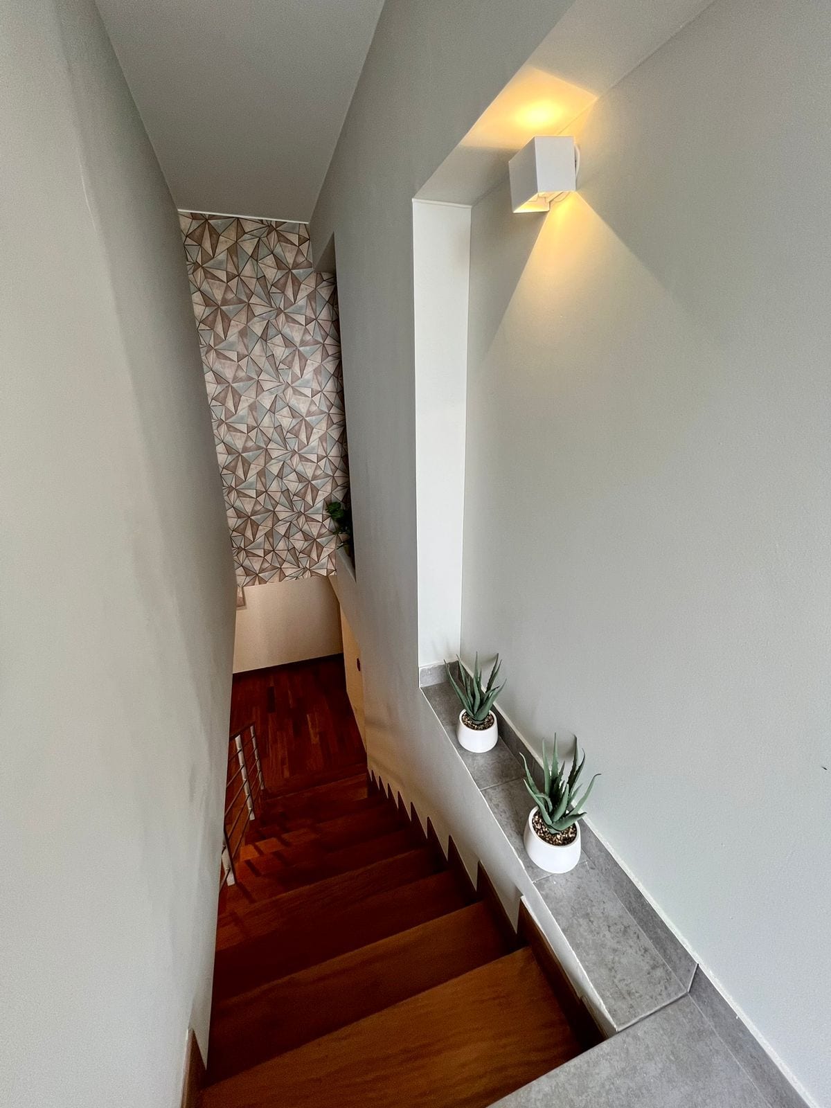 Una escalera con una pared de diseño geométrico, una lámpara y plantas en macetas.