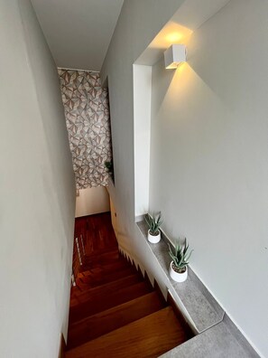 Una escalera con una pared de diseño geométrico, una lámpara y plantas en macetas.