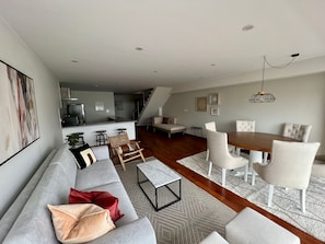 Un espacio habitable moderno con sofá, mesa de comedor y sillas, una zona de cocina y una escalera que lleva a un nivel superior.