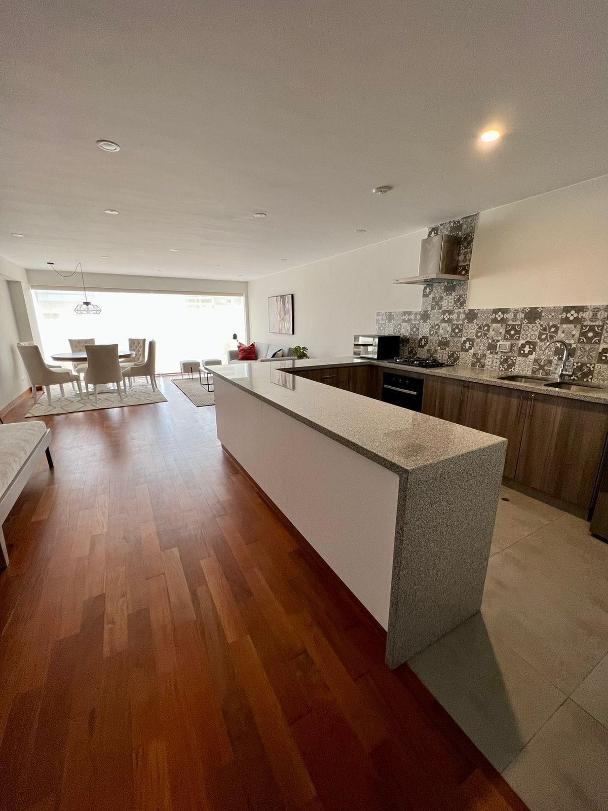 Una cocina moderna con una isla central, suelo de madera y un comedor con mesa y sillas.