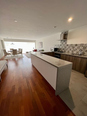 A modern kitchen with a central island, wooden flooring, and a dining area with a table and chairs. - Walk to Larcomar | Peaceful 7th Floor Flat • AC (Miraflores)