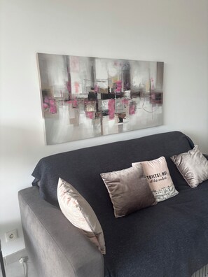 Ein modernes Wohnzimmer mit einem grauen Sofa, zwei Zierkissen und einem großen, abstrakten Gemälde an der Wand.