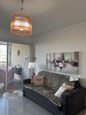 Un salon moderne avec un canapé, une table basse en verre, un luminaire suspendu et un grand tableau abstrait accroché au mur.