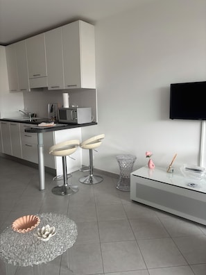 Une cuisine moderne avec des meubles blancs, un four à micro-ondes et un téléviseur noir fixé au mur.