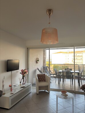 Ein modernes Wohnzimmer mit Flachbildfernseher, einem weißen Sofa, einem Glastisch und einem Essbereich mit Stühlen und Tisch.