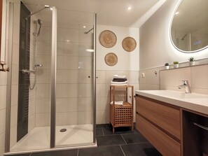 A modern bathroom with a glass-enclosed shower, a wooden vanity, and decorative wall art. - New Listing (Malchow)