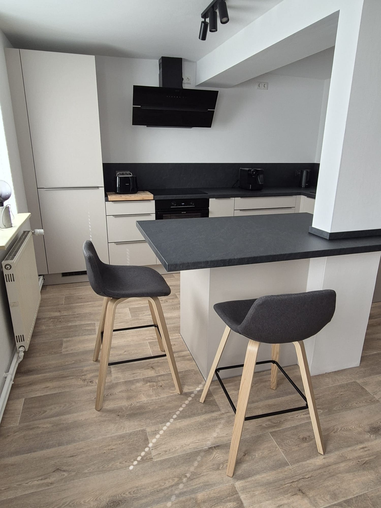 A modern kitchen with a black countertop, two bar stools, and a built-in oven.