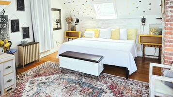 Una camera da letto con un letto, comodini, una panca, un termosifone e un tappeto decorato.
