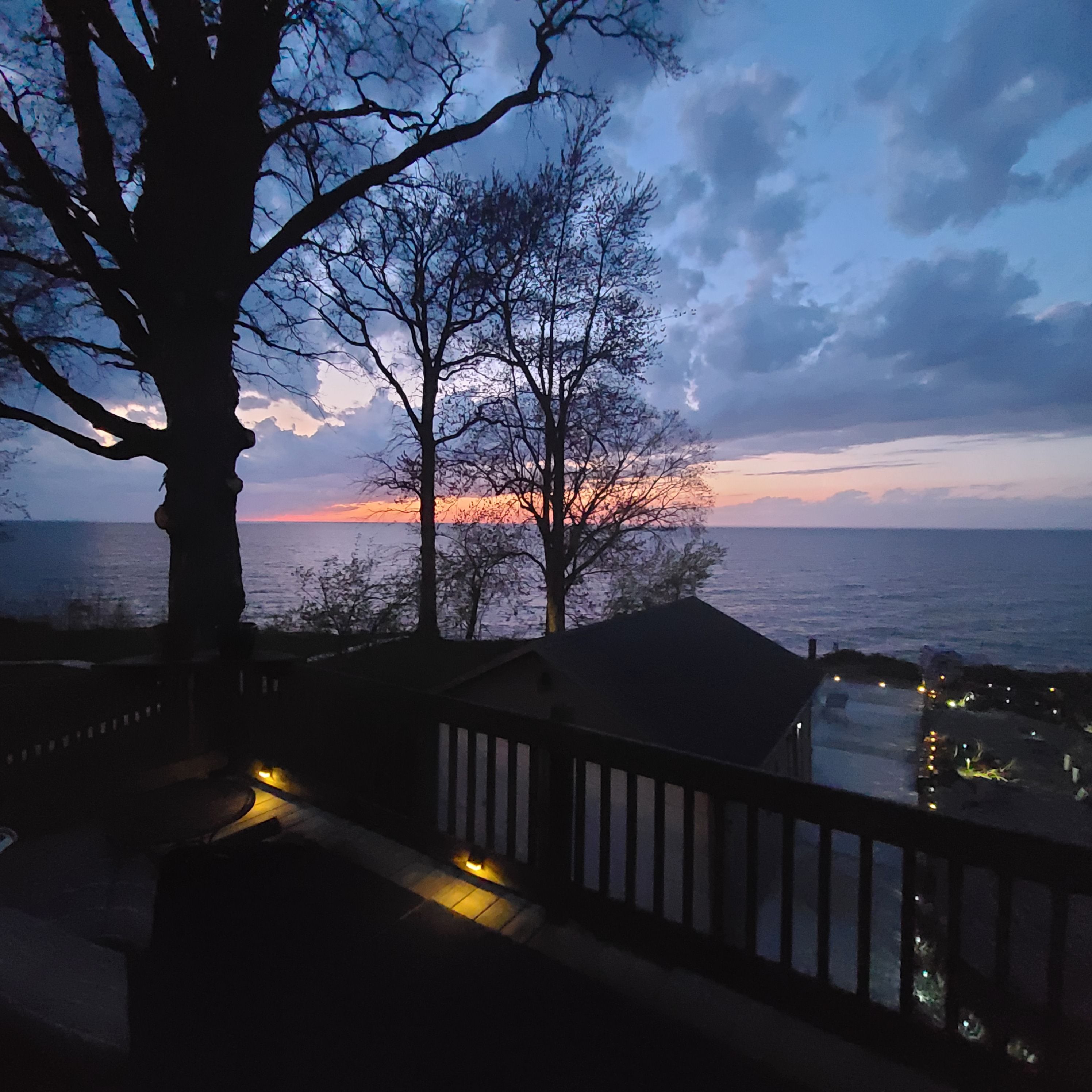 A balcony overlooking a sunset with a tree and a railing.