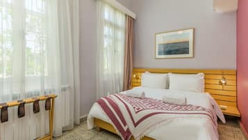 A hotel room with a bed, a window with sheer curtains, a wooden headboard, a wall-mounted picture, and a bedside lamp.