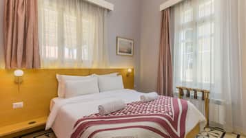 A hotel room with a bed, curtains, a headboard, a wall-mounted light, and a radiator.