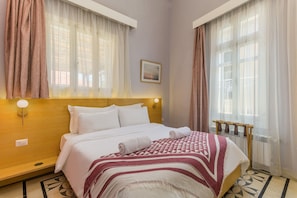 A hotel room with a bed, curtains, a headboard, a wall-mounted light, and a radiator. - Breathe Batroun by Stayinn (Batroun)