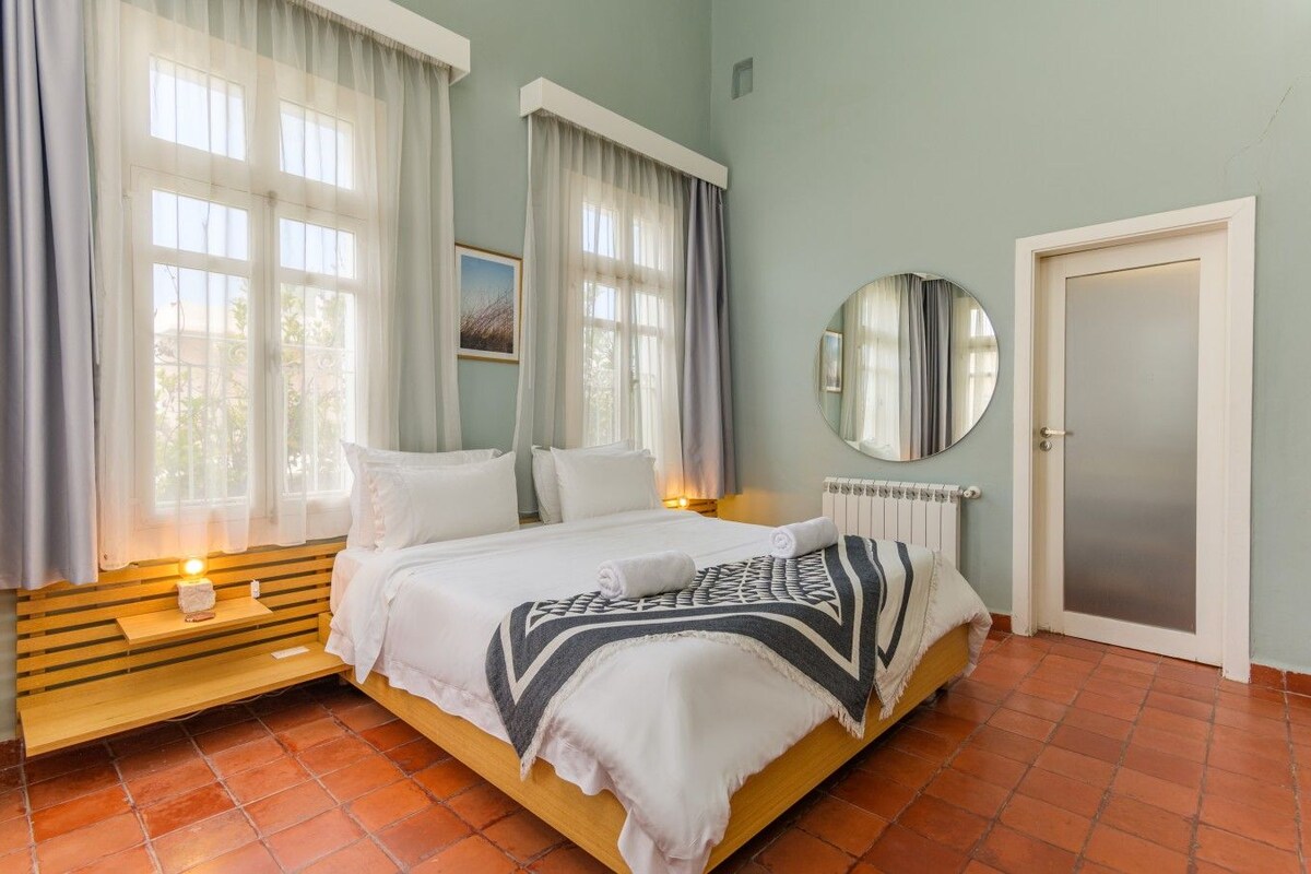 Een slaapkamer met een bed, nachtkastje, spiegel en deur.