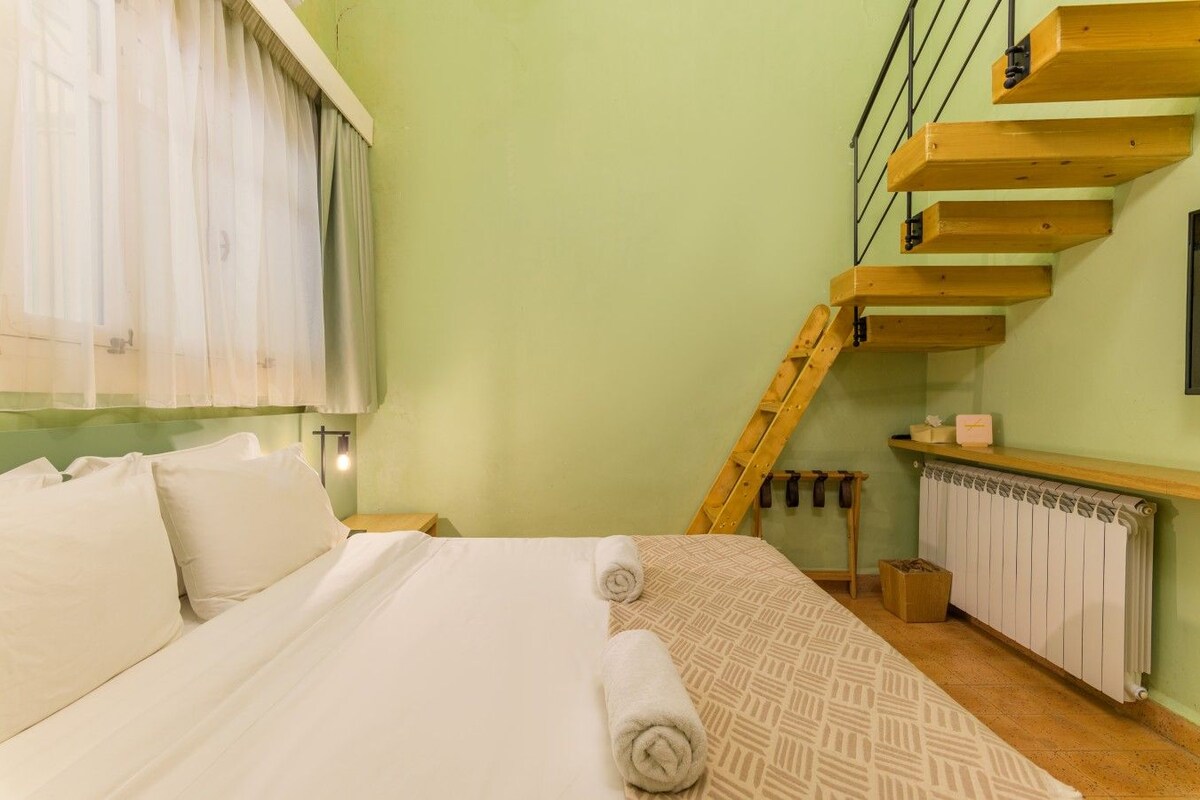 Een slaapkamer met een bed, een raam met gordijnen, een houten trap en een radiator.
