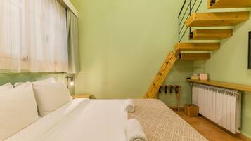 Um quarto com cama, janela com cortinas, escada de madeira e radiador.