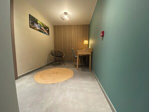 Une petite pièce avec un tapis rond en fibres tressées, une chaise, une table, un tableau accroché au mur, un luminaire au plafond et un feu rouge d’éclairage de sécurité.