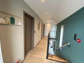 Un couloir avec un escalier, une porte et un luminaire fixé au mur.