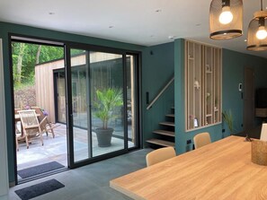 Un intérieur moderne avec une porte-fenêtre coulissante donnant sur un patio, une table à manger en bois et un escalier doté d’une étagère intégrée.