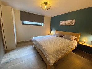 A bedroom with a bed, bedside lamps, a window with blinds, and a wall-mounted artwork. - New Listing (Hotton)