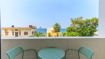 A balcony with two chairs and a small table, overlooking a coastal view with buildings and trees.