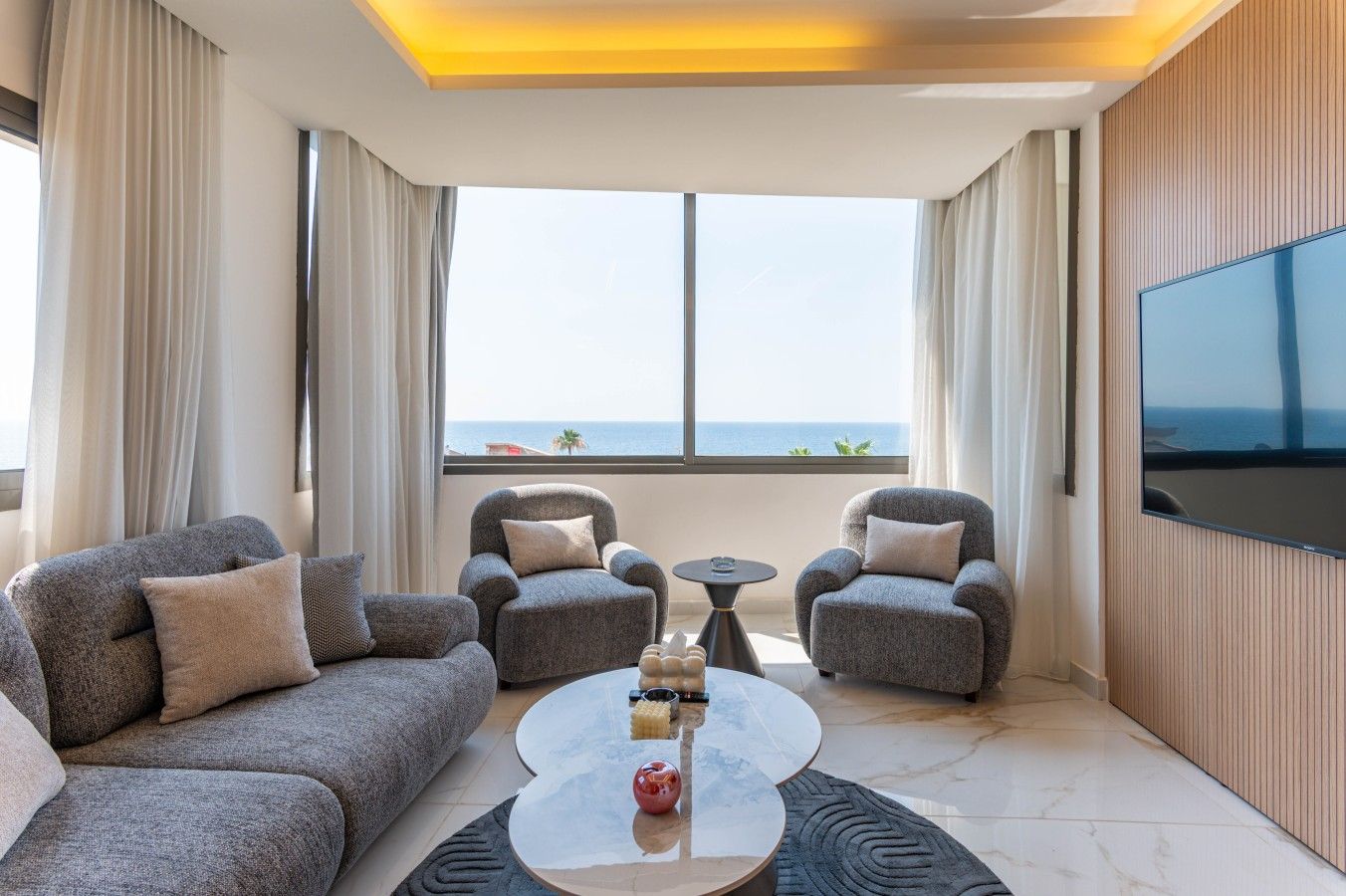 A modern living room with grey sofas, a coffee table, and a TV mounted on the wall.