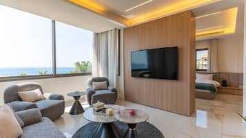 A modern hotel room with a large TV, comfortable seating, a view of the sea, and a balcony.