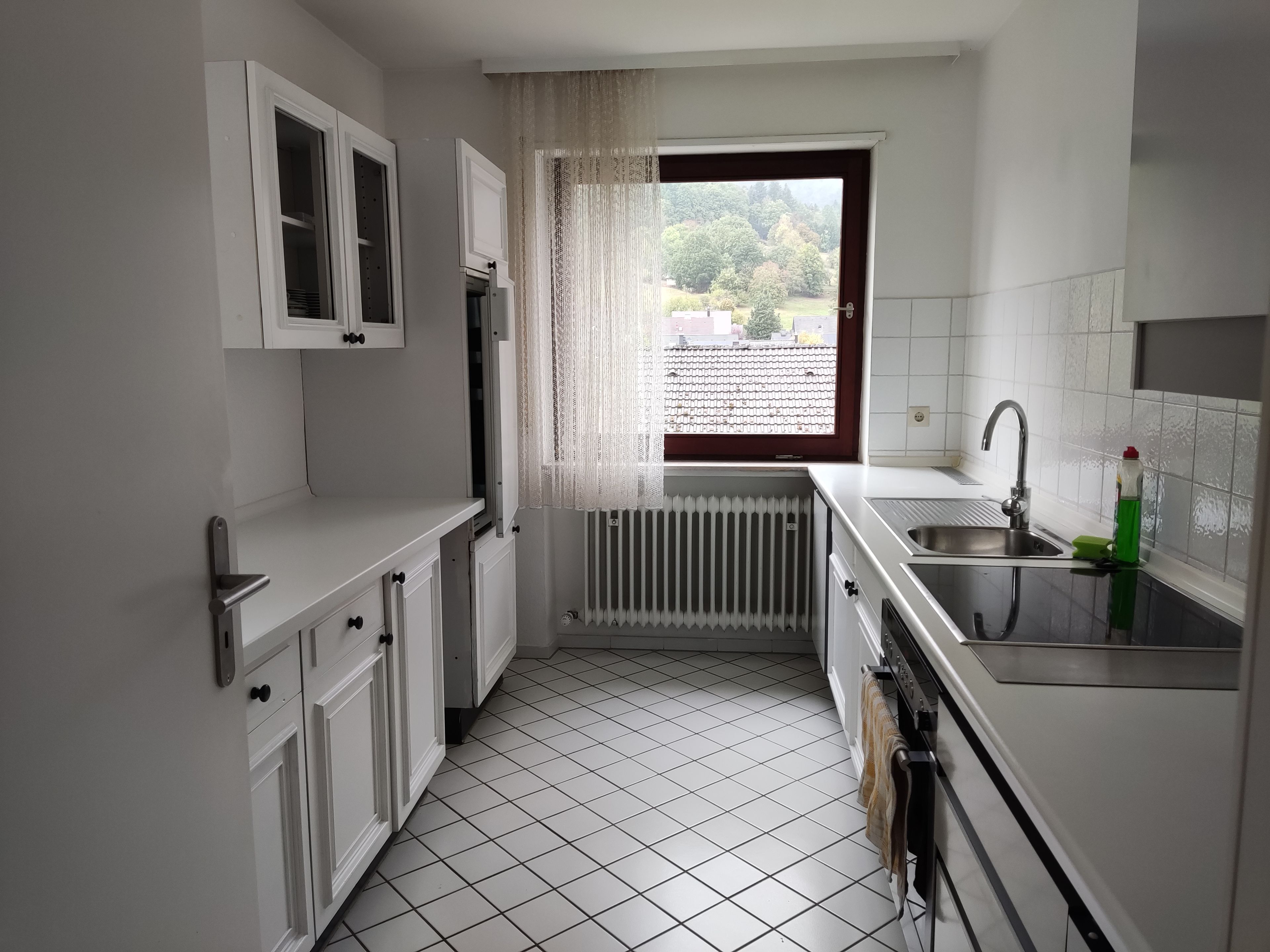 Eine kompakte Küche mit weißen Schränken, einem Fenster mit Aussicht und einem gefliesten Boden.