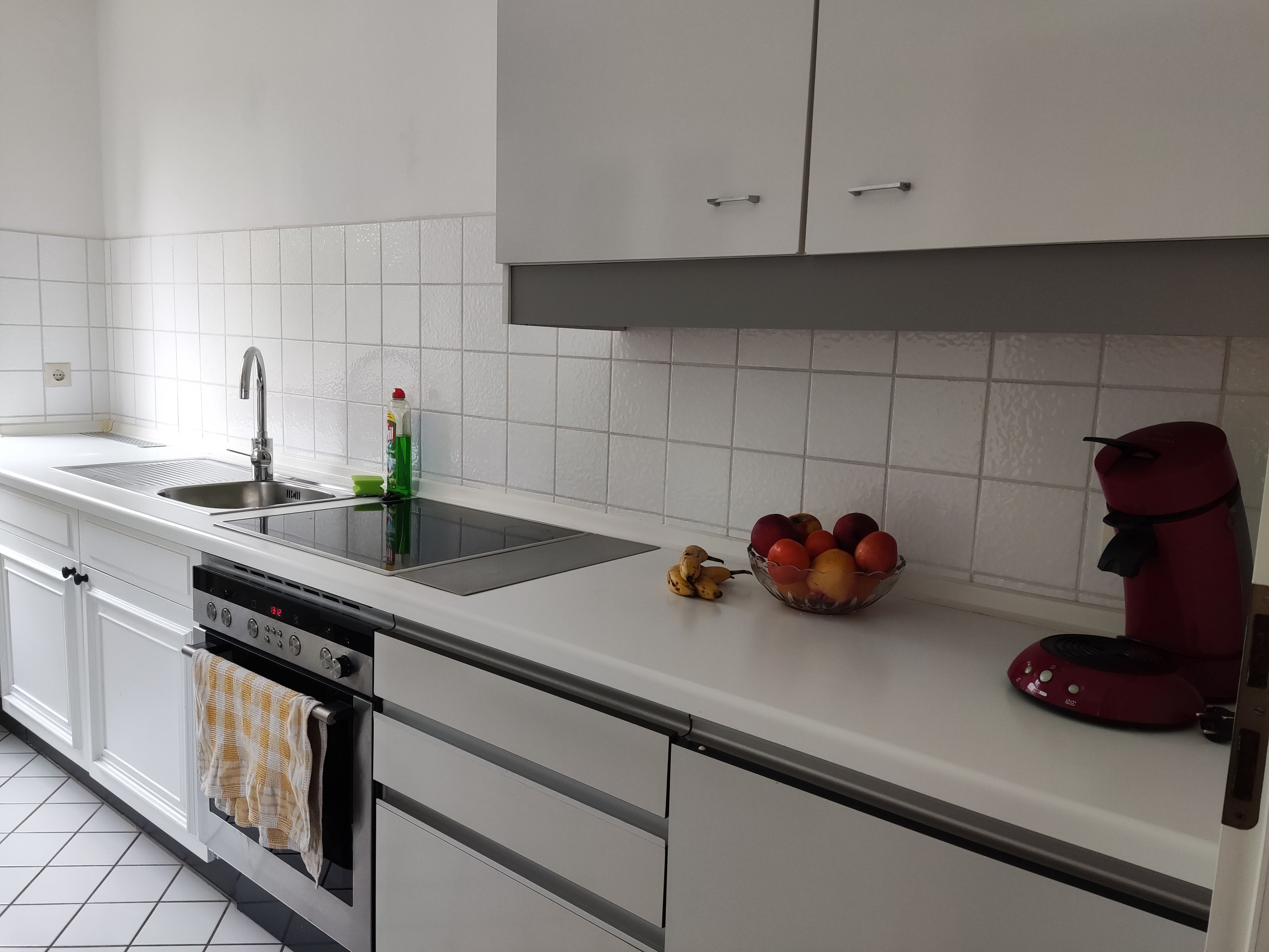 A modern kitchen with white cabinets, a stainless steel sink, a dishwasher, and a red coffee machine.