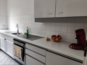 Une cuisine moderne avec des meubles blancs, un évier en acier inoxydable, un lave-vaisselle et une machine à café rouge.
