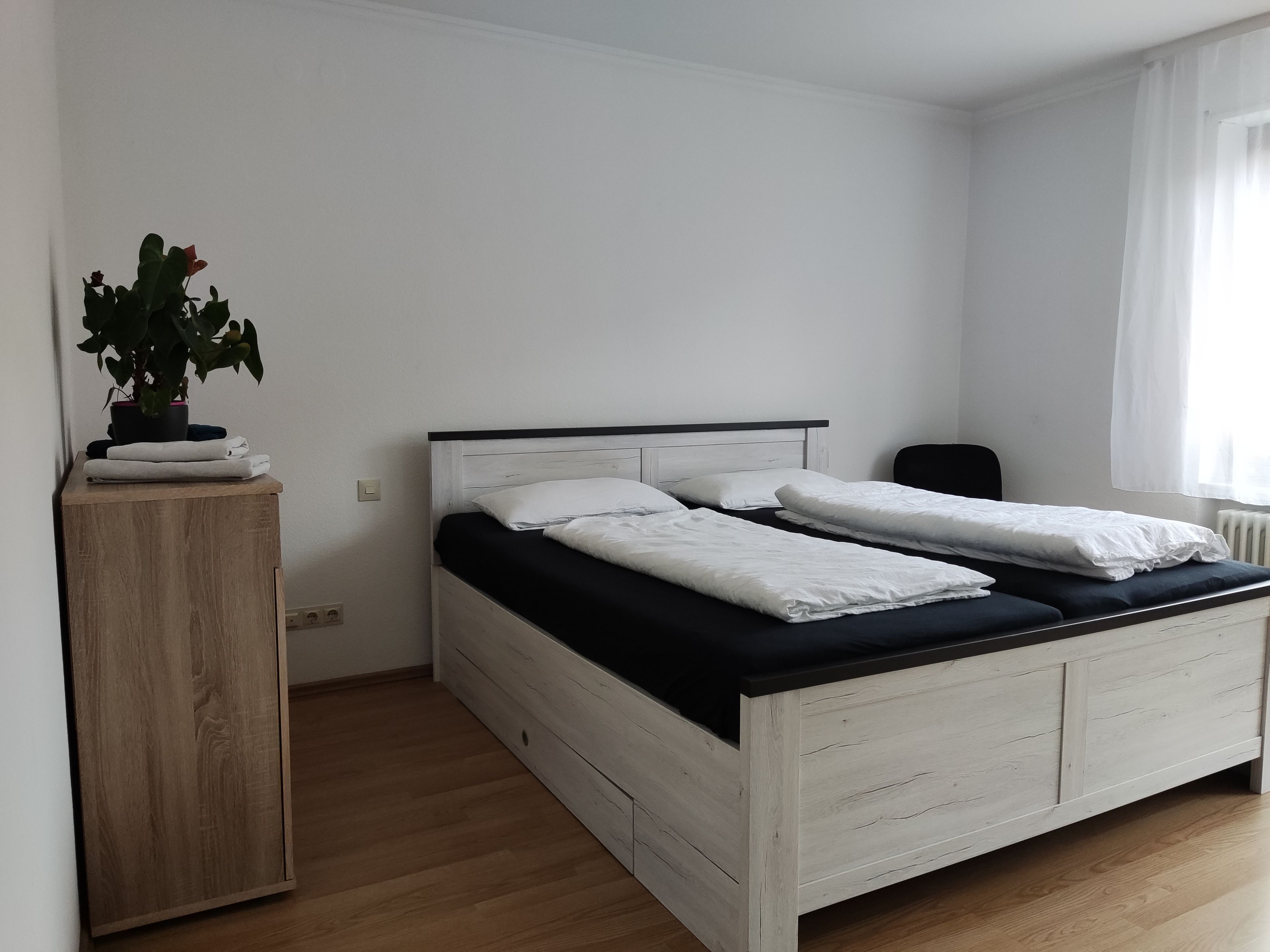Ein Einzelbett mit hölzernem Kopfteil, ein Nachttisch mit einer Pflanze und eine Heizung.