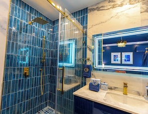 Un baño moderno con ducha envuelta en vidrio, paredes de mármol y tocador con espejo y toallero.