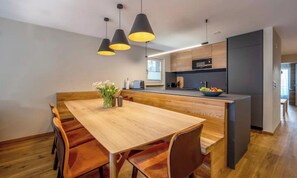 Una cocina moderna con una mesa de comedor de madera, lámparas colgantes negras y un microondas empotrado.