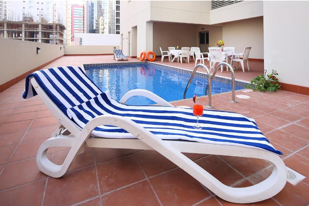 Un área de piscina en la azotea con un sillón de descanso, una mesa junto a la piscina y sillas.