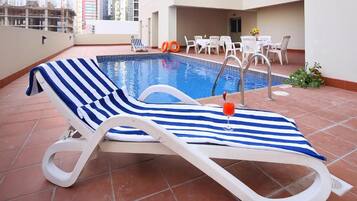 Un área de piscina en la azotea con un sillón de descanso, una mesa junto a la piscina y sillas.