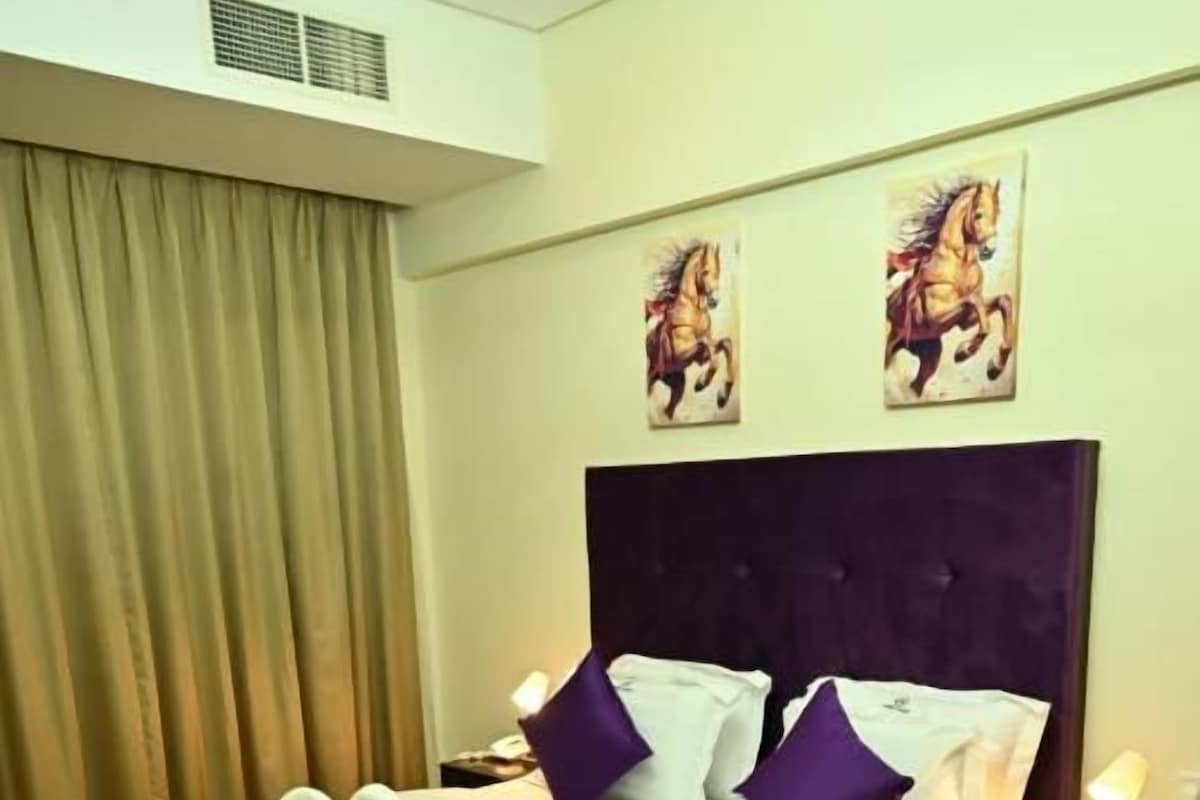 A hotel room with a bed, curtains, artwork, and a nightstand.
