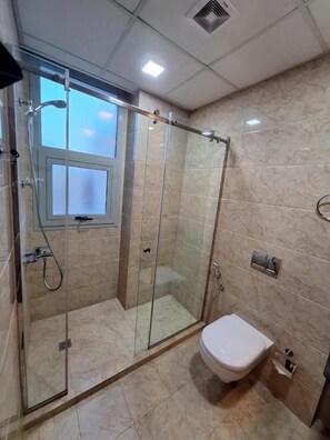 A bathroom with a glass-enclosed shower, a toilet, and a window. - Aspire Tower (Manama)