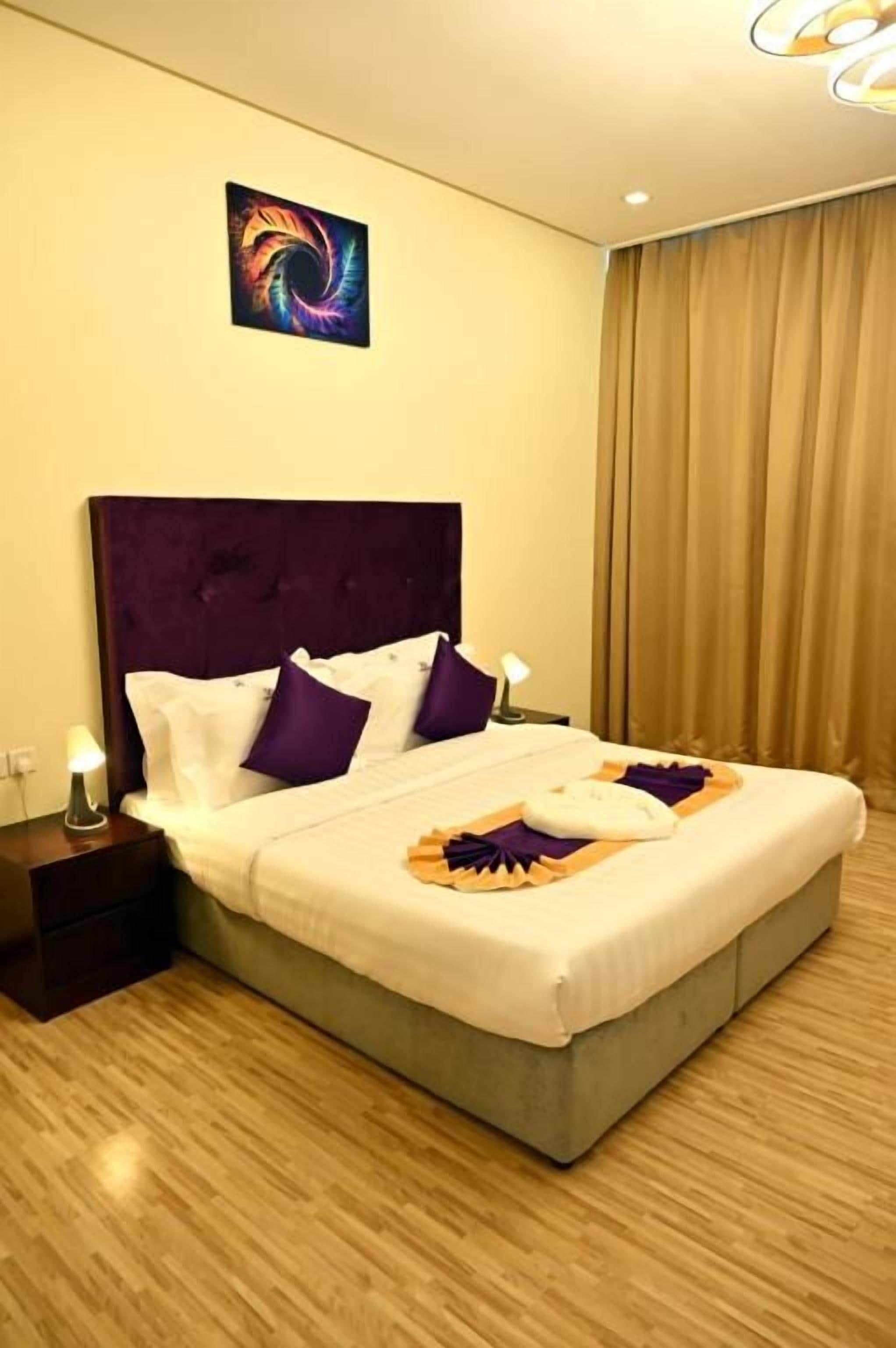 Quarto de hotel com cama grande, cabeceira, mesa de cabeceira com abajur e obra de arte na parede.